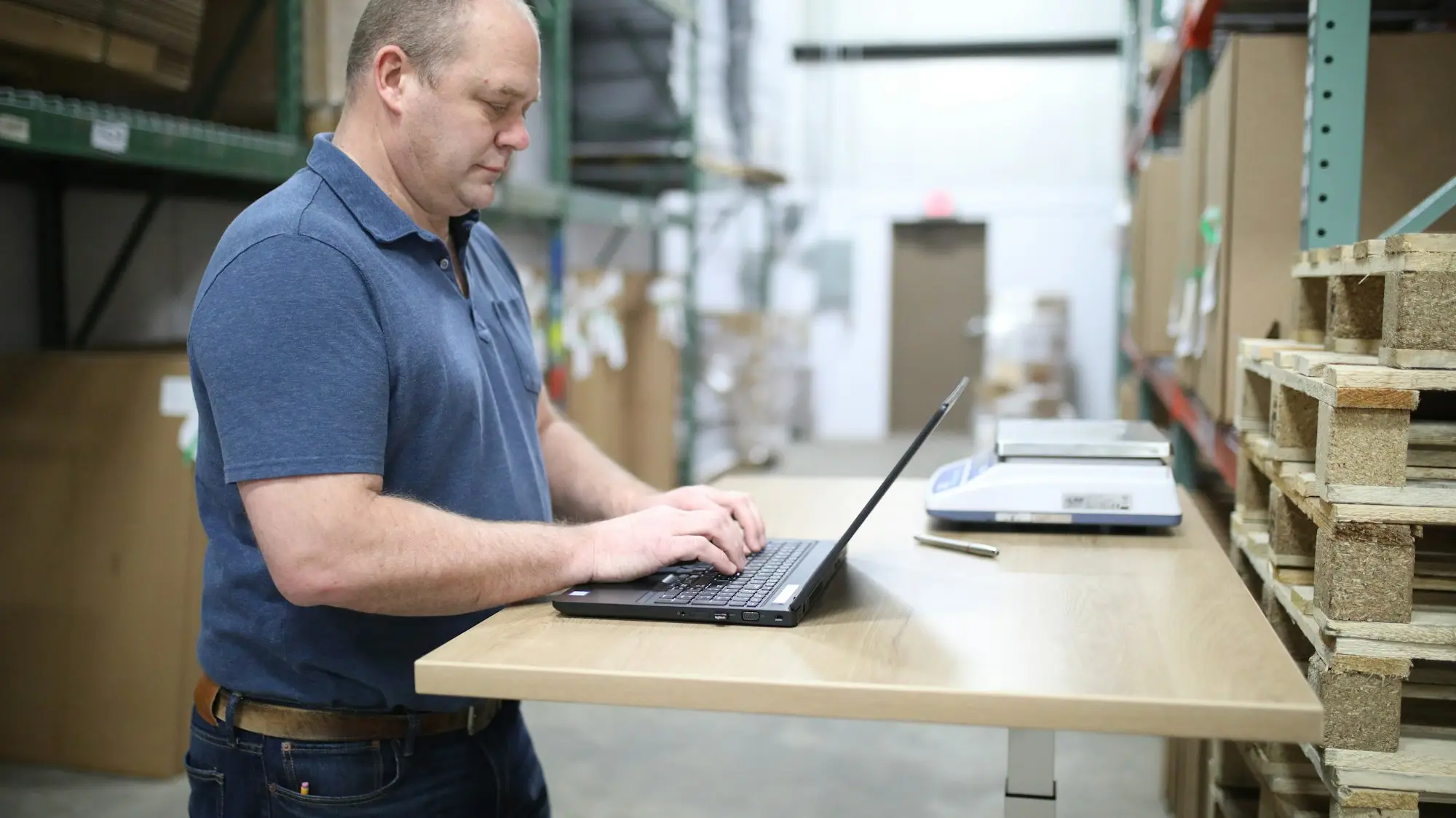 Finance manager reviewing cash flow on a laptop at a standing desk in a warehouse